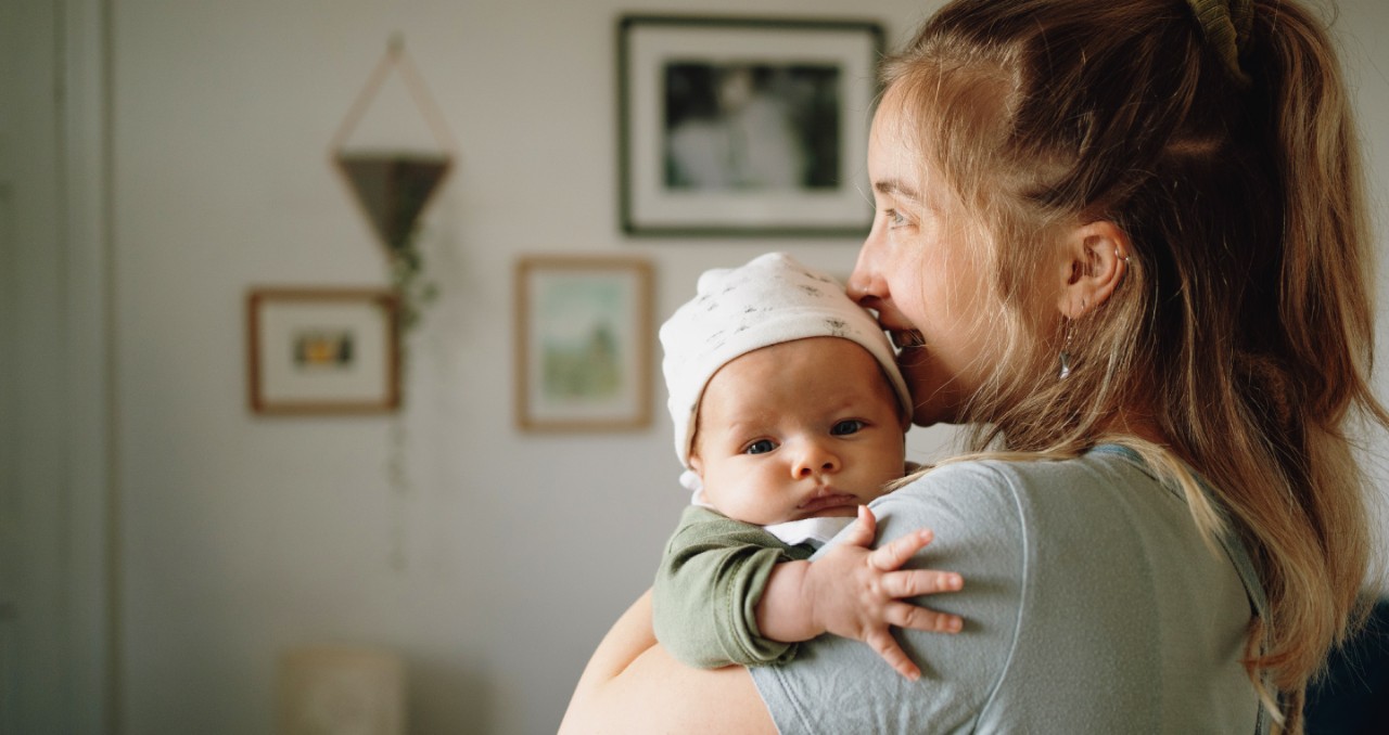A young mother holds an infant who is looking into camera
