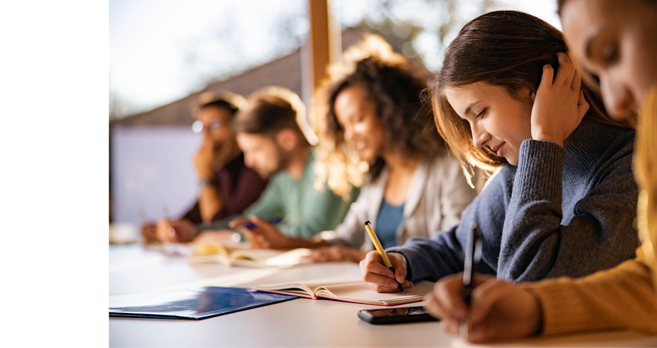 Teenage students at desk writing in notebooks