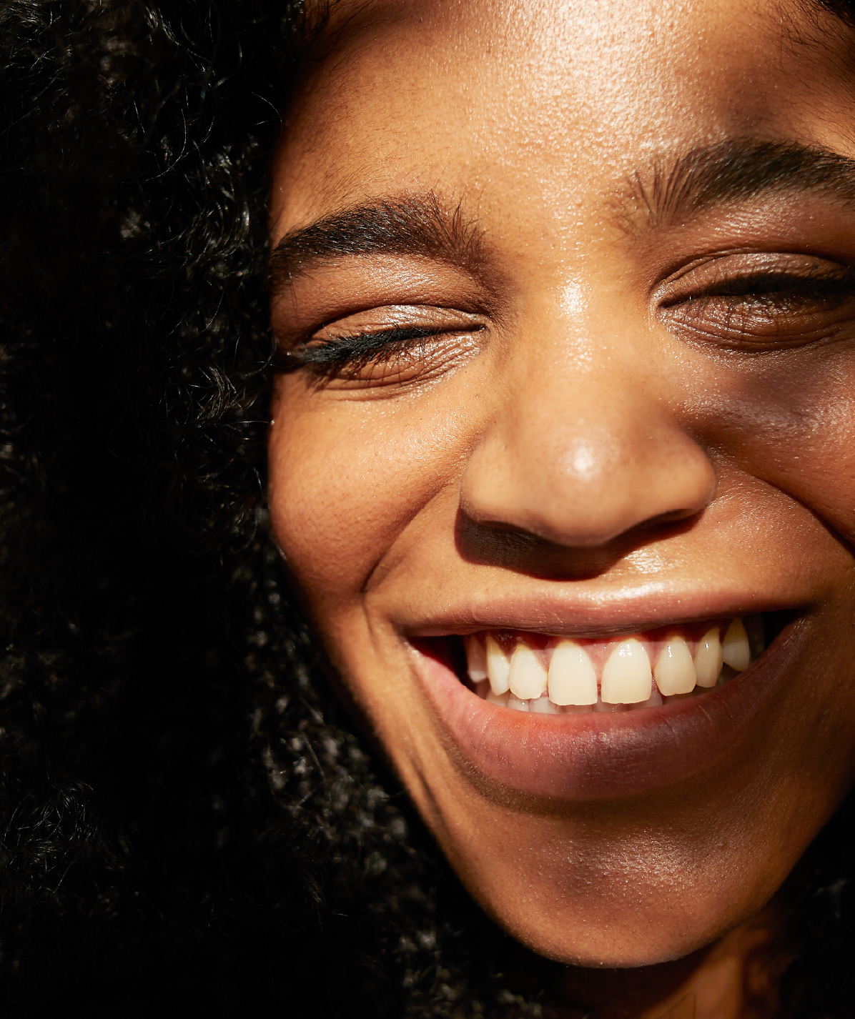 An African American woman smiles and squints basked in light
