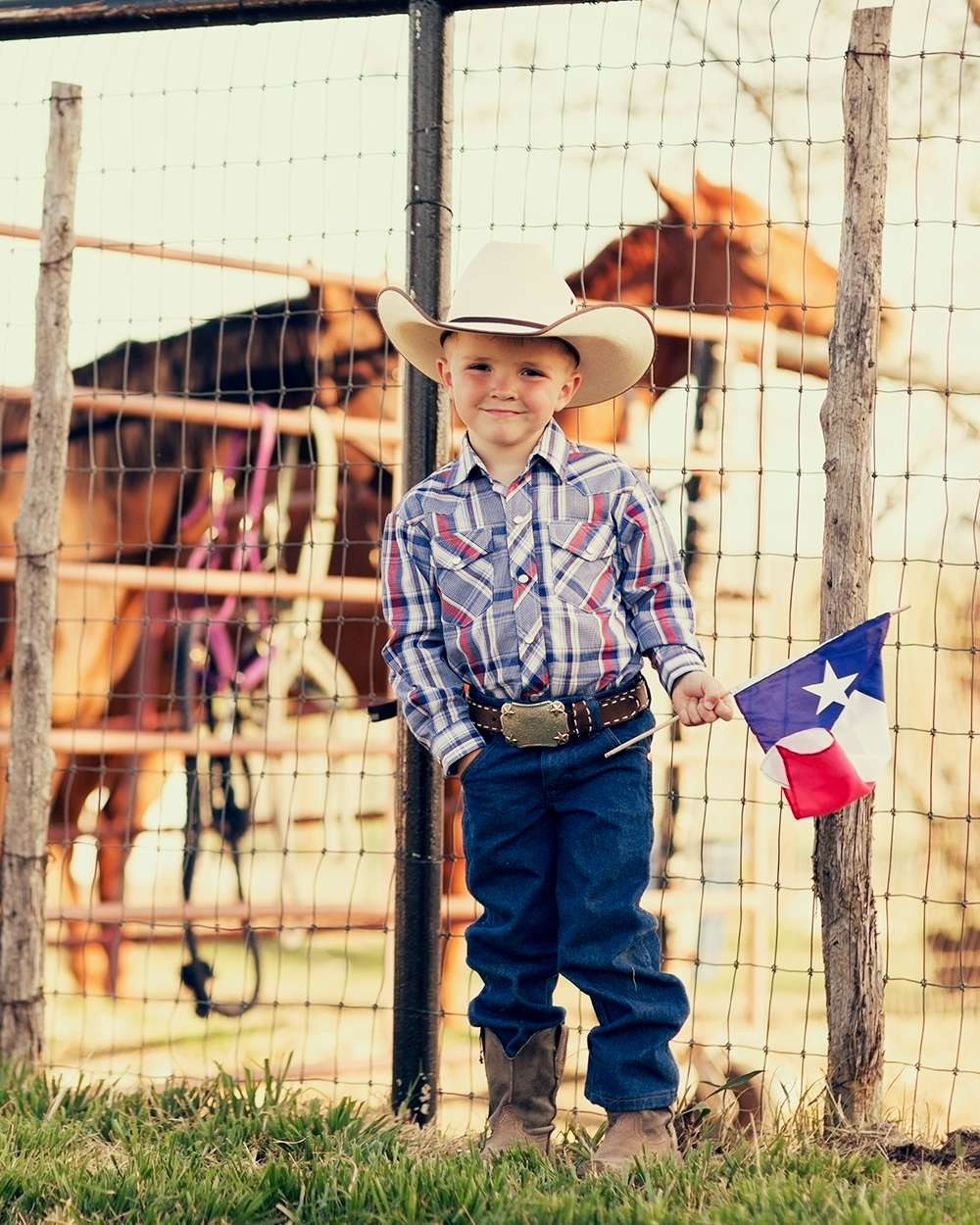 A young cowboy is proud to display the flag of Texas.
