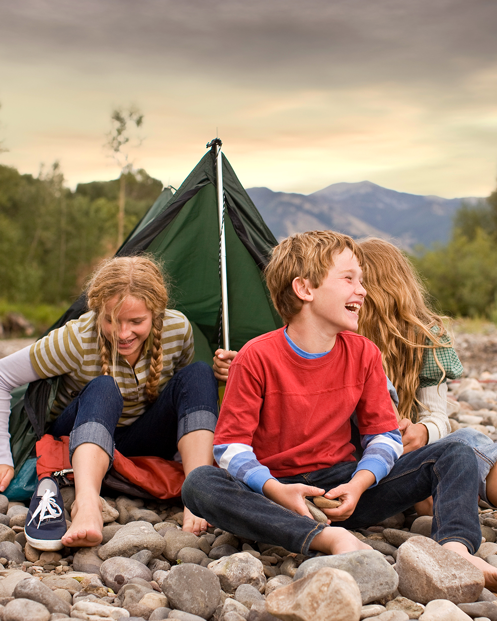 Brother and sisters playing outdoors around small pup tent along a creek