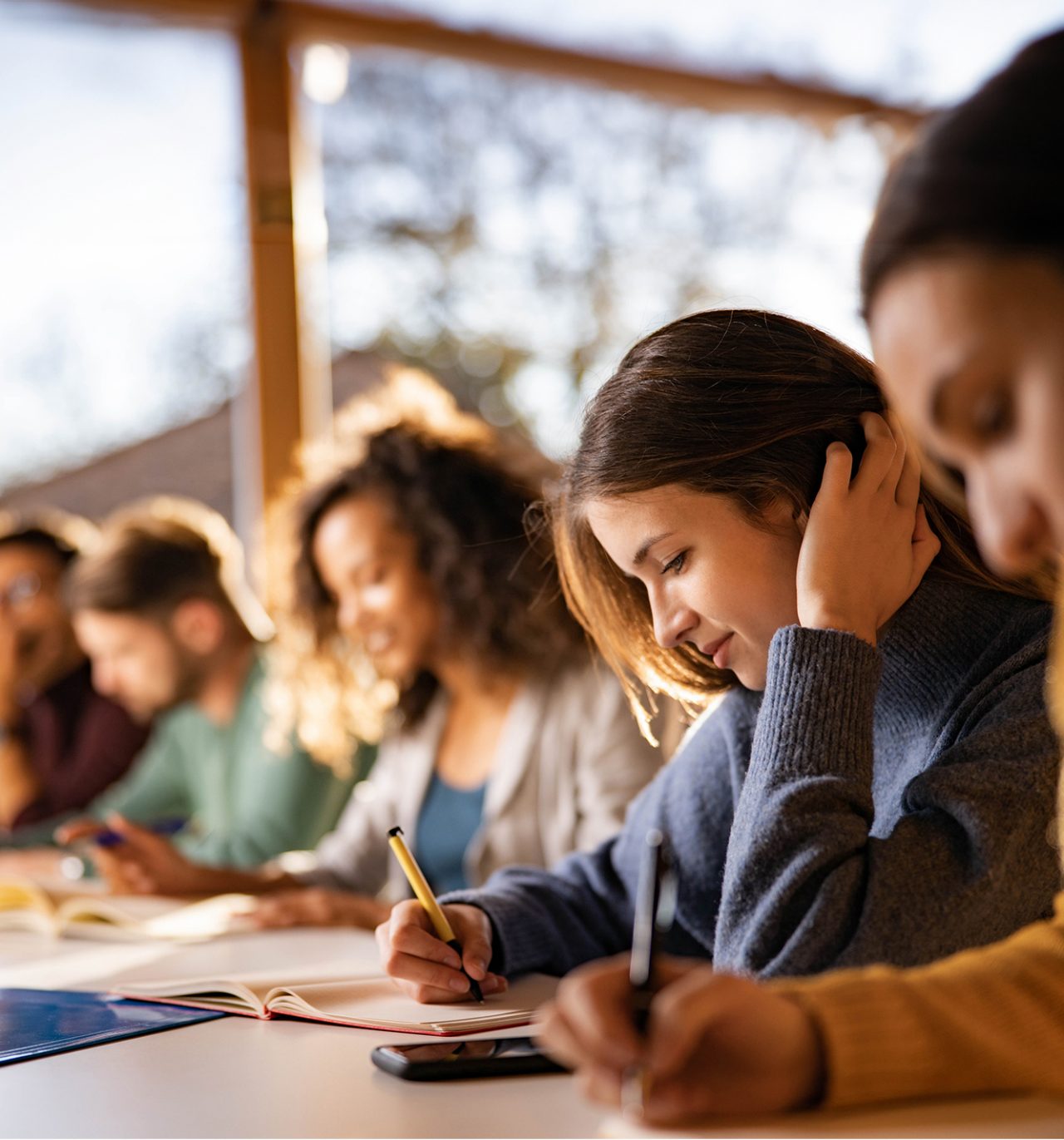 Teenage students at desk writing in notebooks