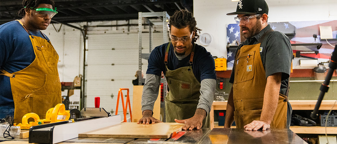 two men stand with table saw cutting wood