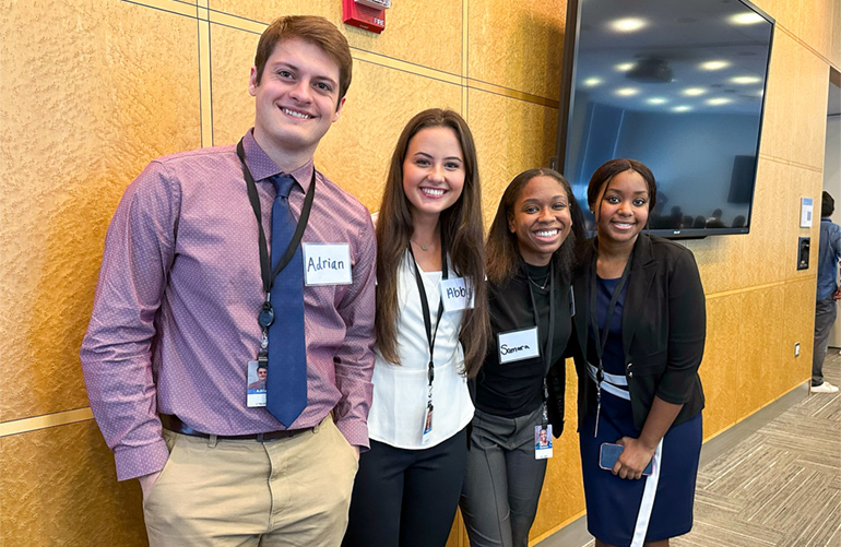 four young interns standing in a line smile